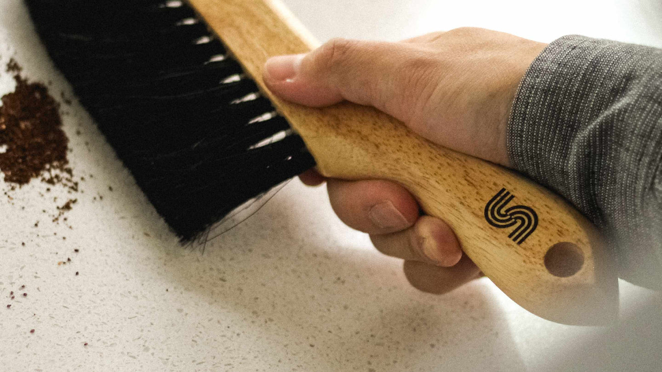 someone sweeping coffee grounds off a counter with a supergood counter brush